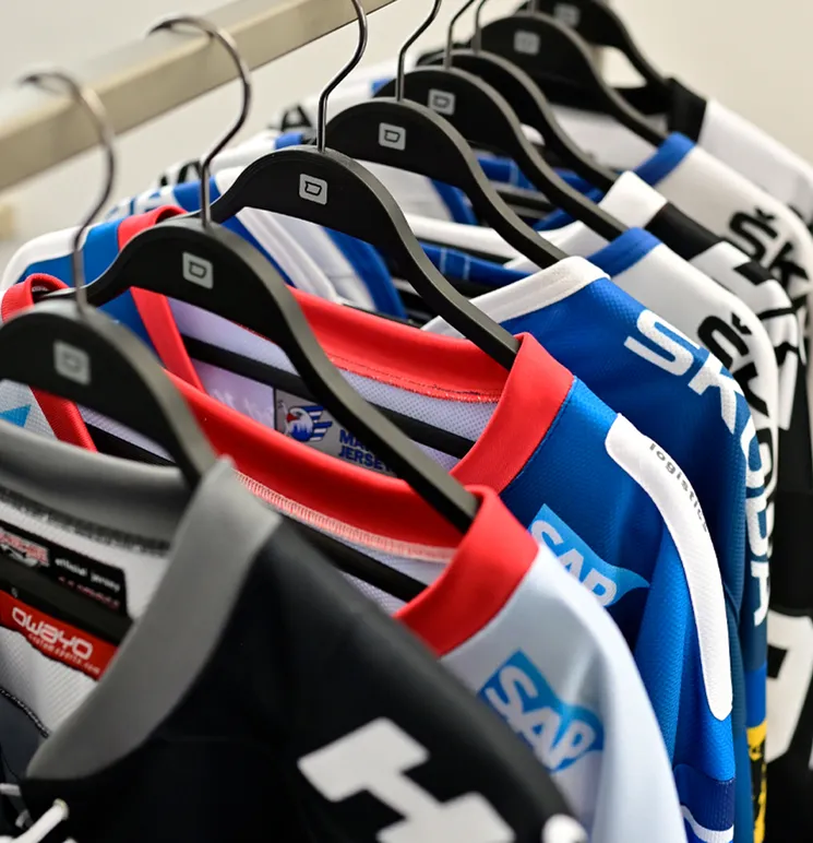 A row of colorful, customized sportswear jerseys from owayo hangs on black hangers on a clothing rack.