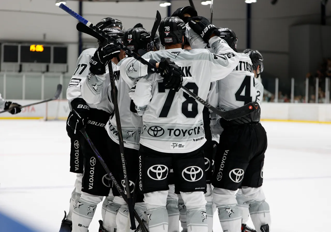 Hockey players in white jerseys with black numbers and sponsor logos hugging on the ice.