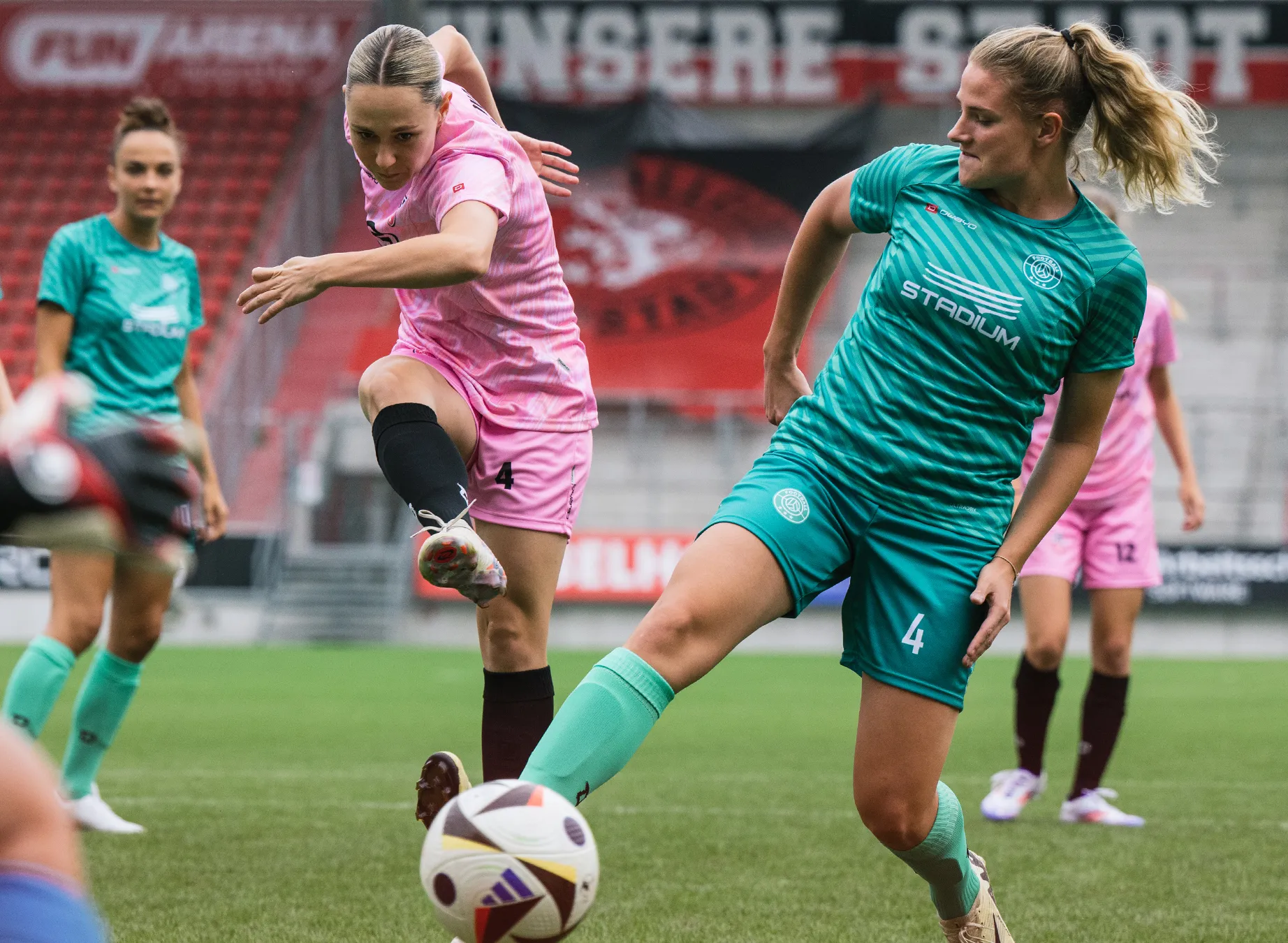 Two women in colorful sports jerseys are playing soccer on a grassy field.