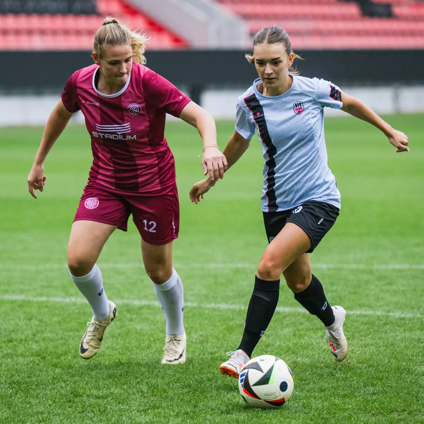 Two women in sportswear are playing soccer on a green field.