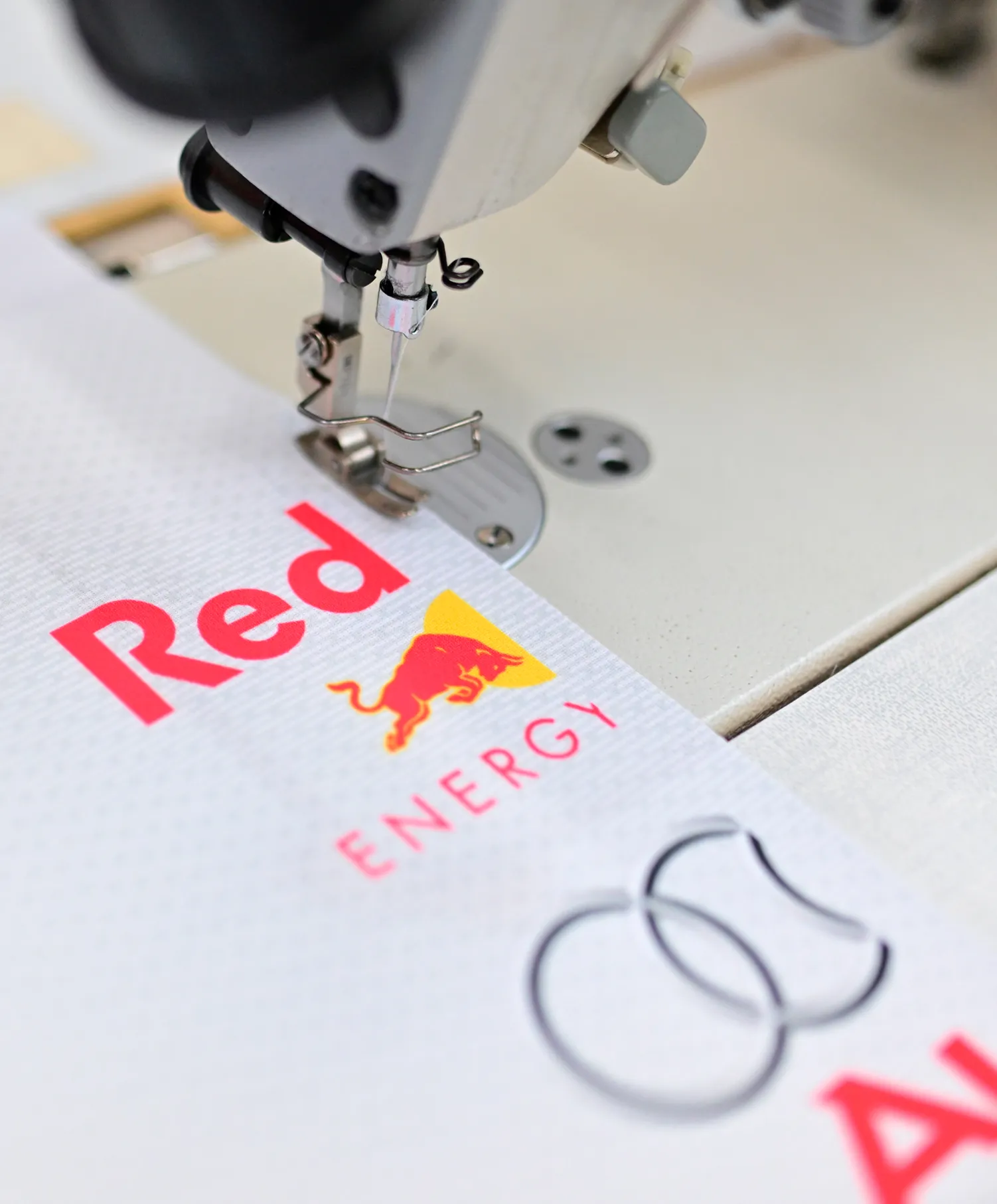 A sewing machine is stitching a white sportswear piece with the Red Bull Energy logo.