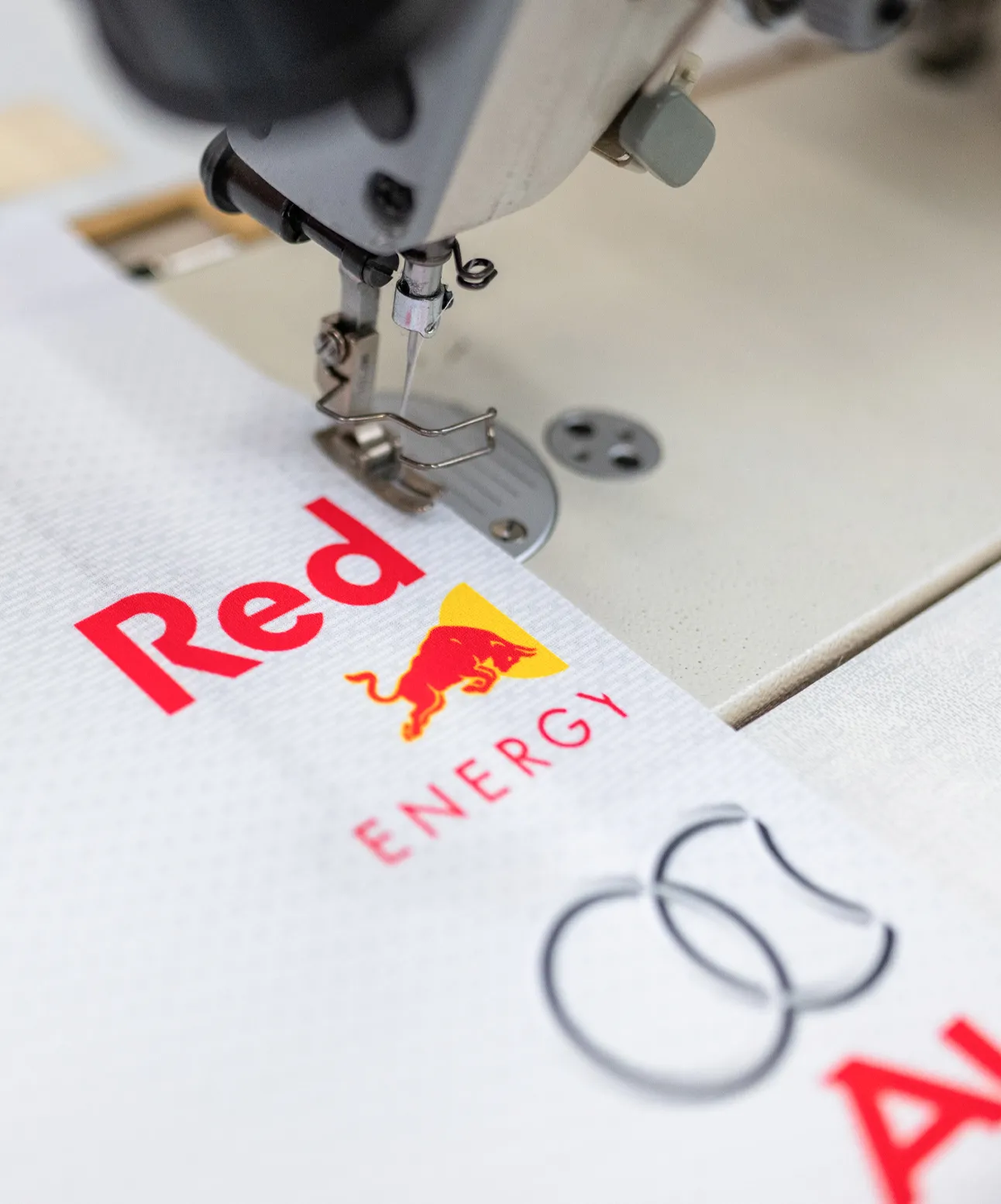 A sewing machine is working on a piece of fabric with printed logos and text.