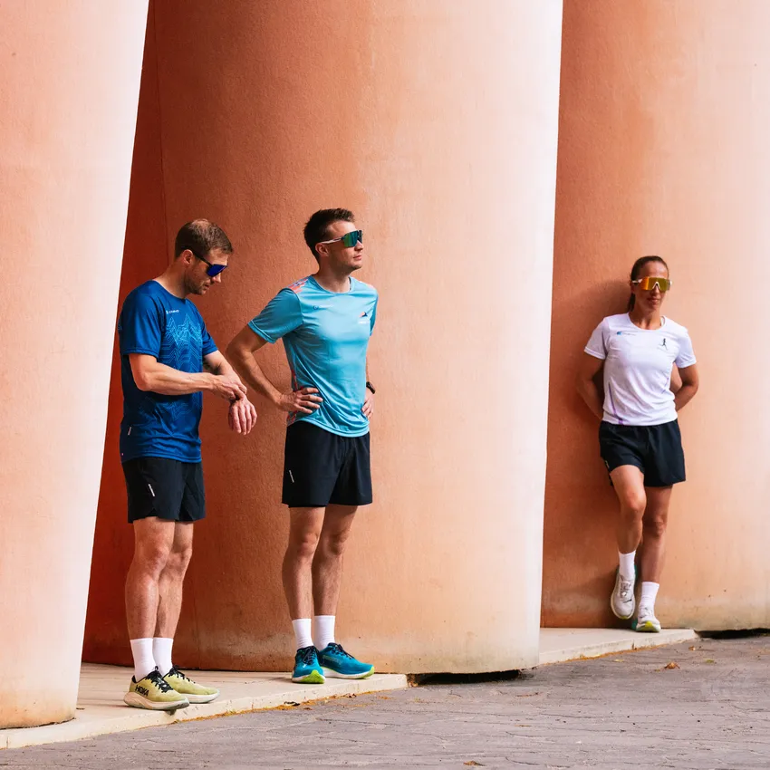 Three athletes in sportswear and sunglasses are casually leaning against pink columns.