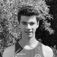 A young man wearing a black and grey sleeveless sports top with the 'owayo' logo on the chest, smiling in front of a background of green leaves.