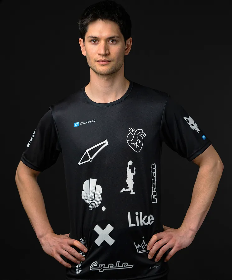 A man is wearing a black sports shirt featuring various white symbols and logos.