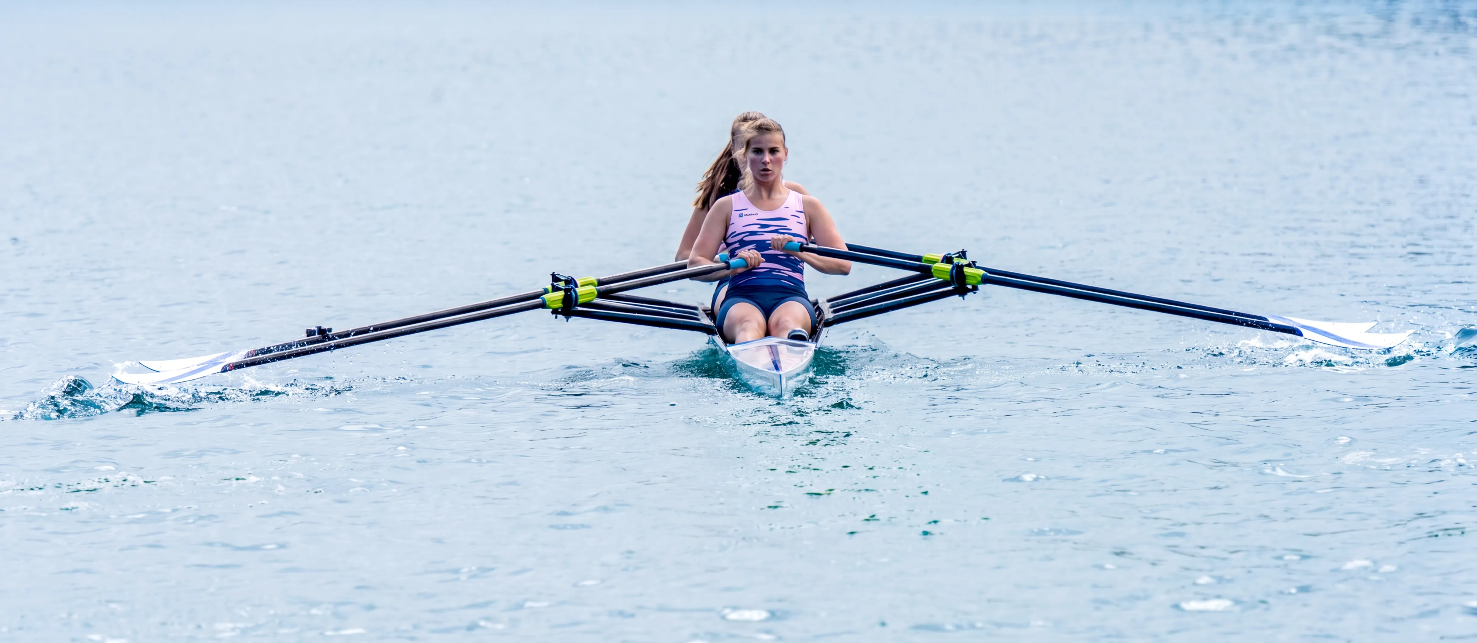 A rower in a boat is paddling across a calm lake.