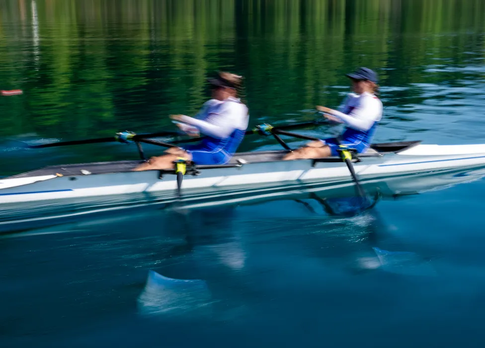 Two rowers in blue sportswear are rowing in sync on calm water.