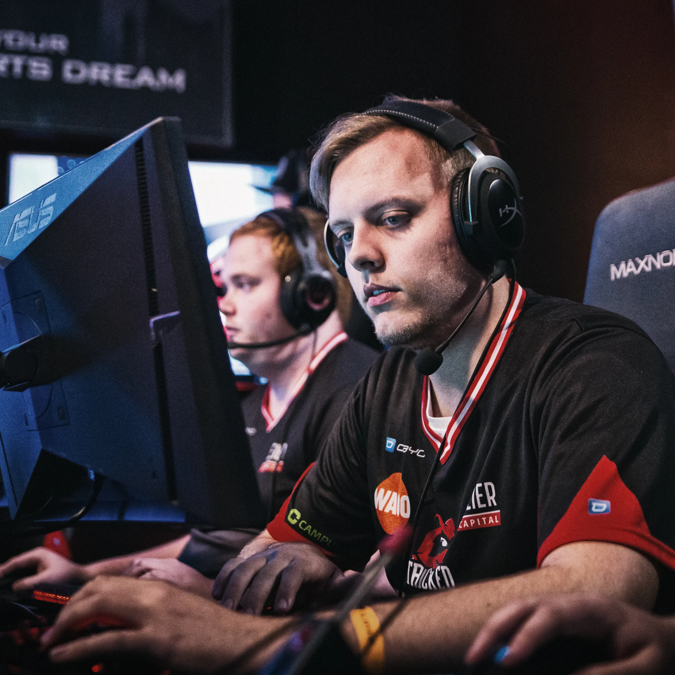 Two players in athletic shirts with headsets, focused on their computers during an eSports tournament.